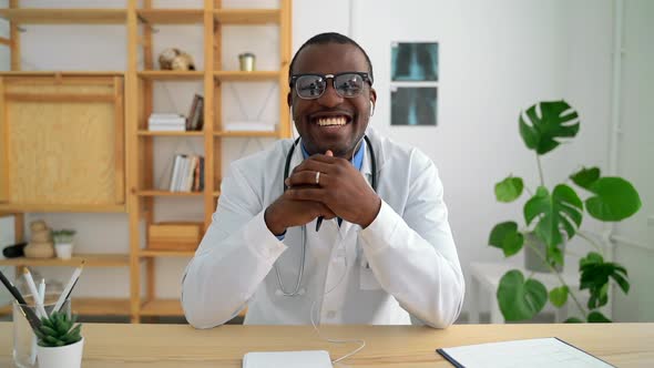 Young Male Doctor Talking and Laughing During Online Conference at Table in Clinic Spbas