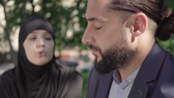 Close-up Side View of Tired Bearded Middle Eastern Man Sighing As Listening To Blurred Muslim Woman