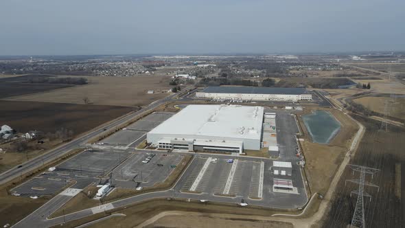 View of industrial park with large buildings and parking lot, farm fields and transmission towers.