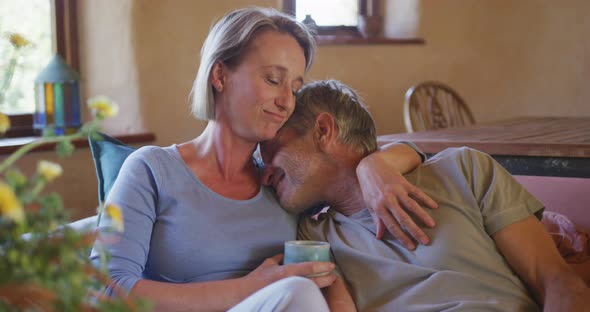 Smiling senior caucasian couple embracing and drinking coffee in living room