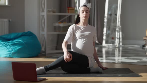 Wide Shot Portrait of Confident Pregnant Young Woman Sitting on Exercise Mat Watching Online Fitness