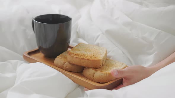 Woman hand eating coffee and bread for breakfast in the bedroom.