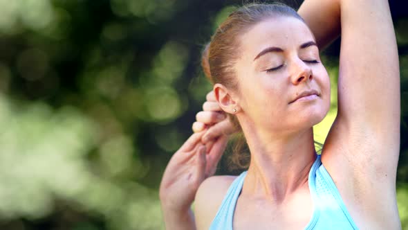 Professional lady athlete with fair hair bun in blue top stretches hands