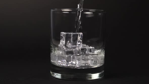 Pouring carbonate mineral water into a glass with ice cubes on a black background 