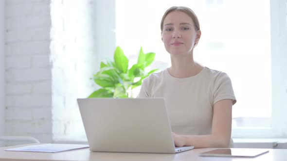 Woman Looking at Camera While Using Laptop