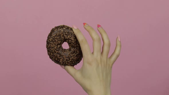 Womens Hand Holding Brown, Delicious, Sprinkled Donut on Pink Background.