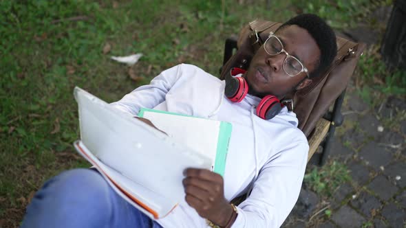 High Angle View of Concentrated African American Genius Man Lying on Bench Studying Outdoors