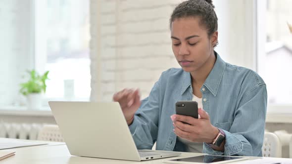 Young African Woman Using Smartphone and Laptop