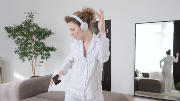 Young Woman Wearing Pajamas Dancing With Mobile Phone At Home