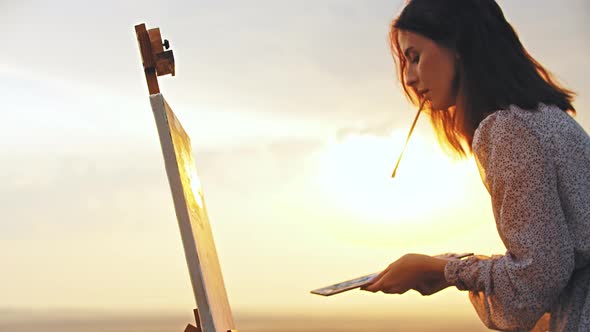 A Young Concentrated Inspired Woman Artist Draws a Painting at Sunset