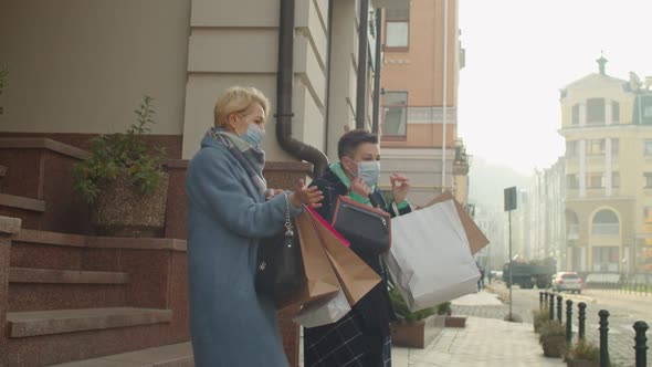 Mature Female Couple with Paperbags Taking Off Medical Masks Outdoors