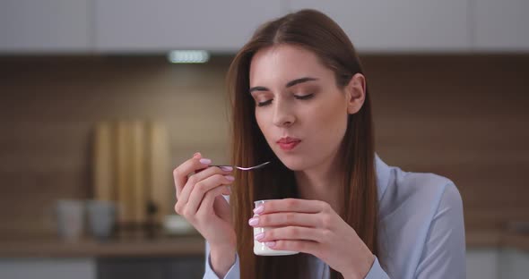 Young Beautiful Girl Sitting in the Kitchen and Eats Yogurt on a Breakfast, Portrait, Day Off at