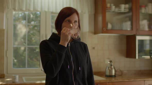 Young Adult Woman Drinking Water Standing in the Kitchen