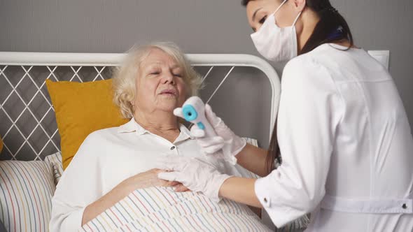 Focus on Senior Woman Lying on Bed While Female Doctor Visiting Her