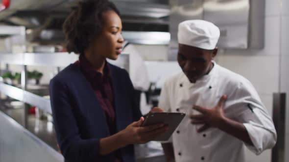 African american female manager using tablet and talking with chef