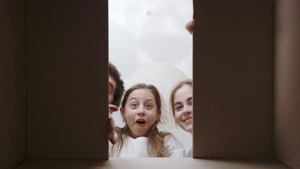 Joyful Kid Opening Cardboard Box Together with Her Parents