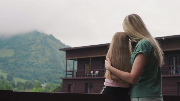 Loving Mother Hugs Little Daughter on Terrace of Eco Hotel