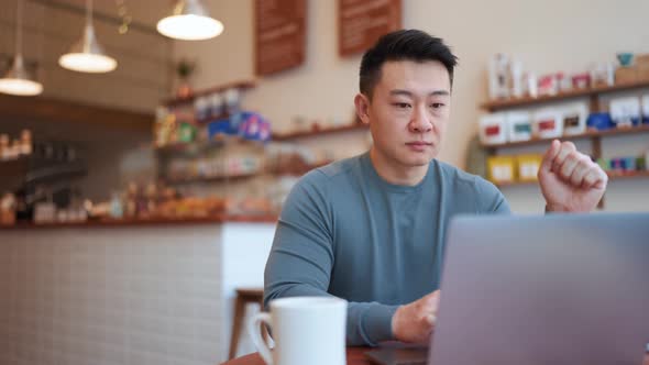 Smiling Asian young man working by laptop and drinking coffee