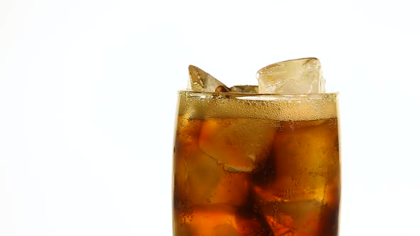 Pouring cola soda water in glass full of ice cubes over white background