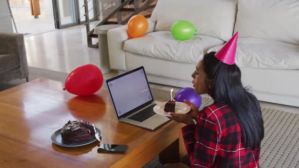 Mixed race woman using laptop having birthday video chat holding a cake