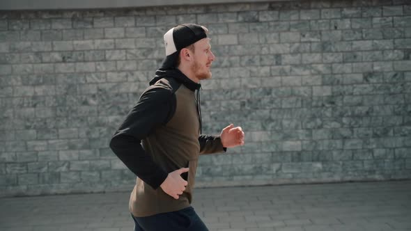 Sportive Athletic Male Runner on Brick Wall Background. Man Jogging Working Out in City. Sportswear