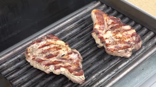 Grilling pork steaks. Delicious juicy meat steaks cooking on the grill. Slow motion 