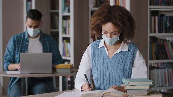 Young Girl Student in Medical Mask Sits at Desk in Library Preparing to Lesson Writing Note in