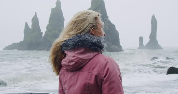 Woman in Raincoat in Mood Rainy Weather Visiting Black Sand Beach with Reynisfjara Sea Stack Cliff