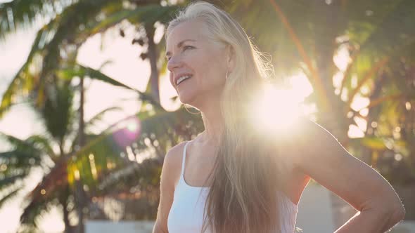 Pretty mature woman looks off screen to left and then to the camera as sun flares behind her in a tr