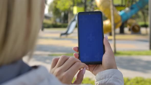 Behind Shoulder View of a Woman Holding a Smartphone with a Screen with a Chroma Key, Browsing