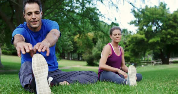 Mature couple performing stretching exercise in the park