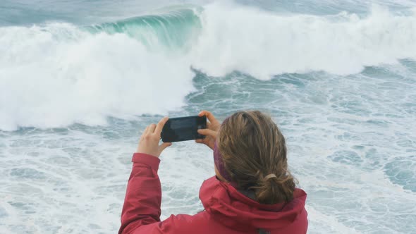 Girl in Jacket Takes Photos on Smartphone of Giant Ocean Waves Slow Motion