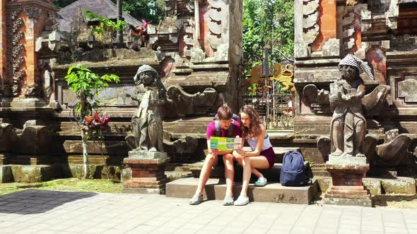 Happy couple sitting on a stone in a beautiful city, reading a brochure with the bright sun shining