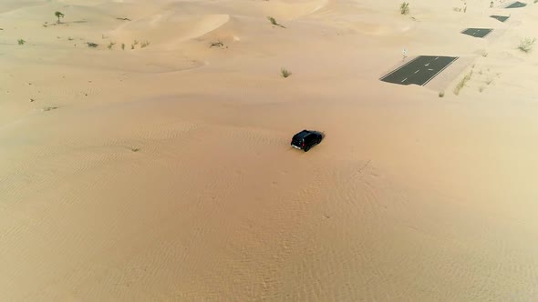 Aerial view of black car driving on road covered by sand, U.A.E.