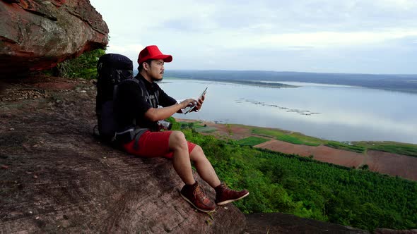 man traveler with backpack looking at the map on the edge of cliff, on a top of the rock mountain