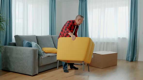 A Man in Home Clothes Assembles a Soft Chair Himself