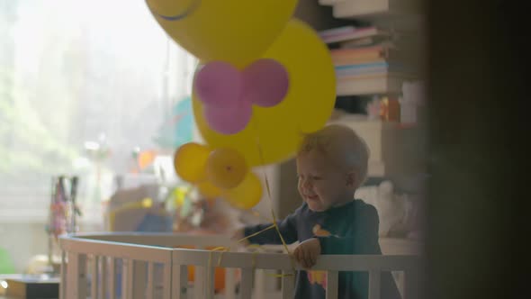 Baby girl playing with balloons in the crib