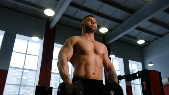 Bodybuilder Makes Distributing of Hands with Dumbbells While Standing in the Gym, Maintaining a