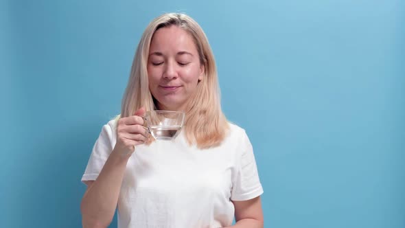 Woman Drinks Glass of Pure Water on Blue Background