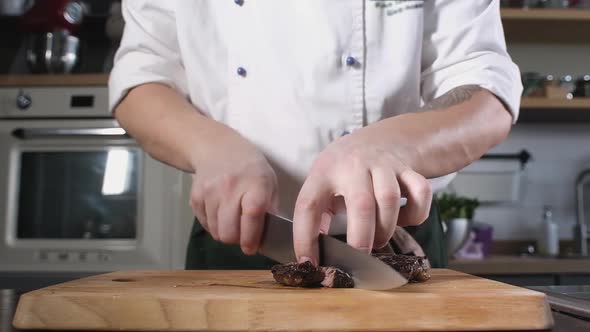 chef cuts cooked steak into pieces with sharp knife on wooden cutting Board.