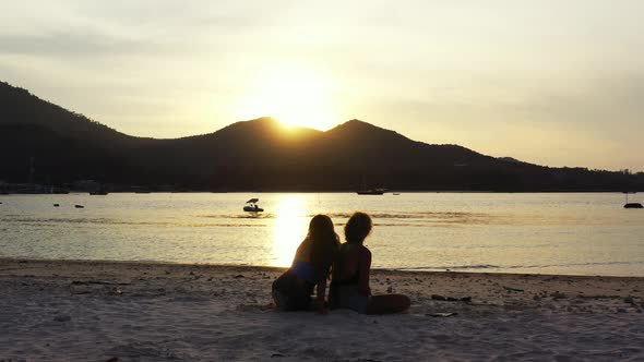 Beautiful golden sun setting behind the mountains. Girls admiring the tropical coast on the golden h