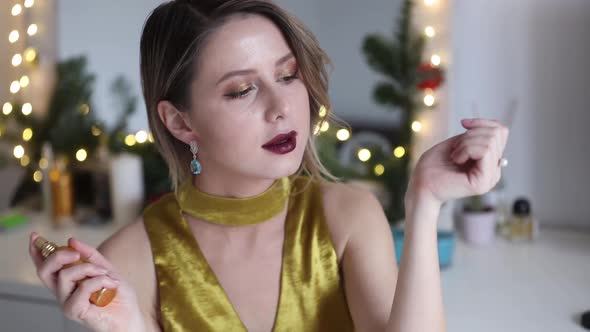 young beautiful woman applying perfume and cosmetics near Holiday decorated mirror at home.