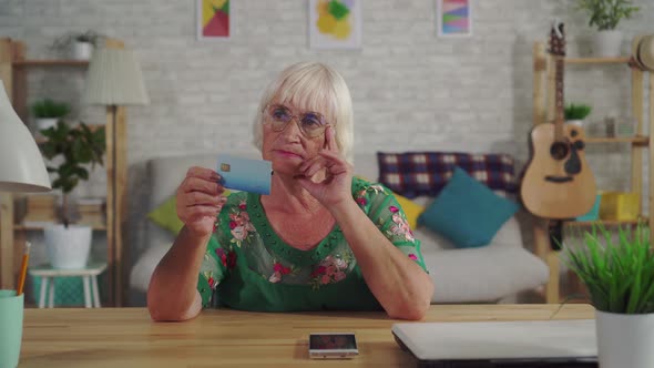 Thoughtful Old Woman with Gray Hair Holds a Bank Card