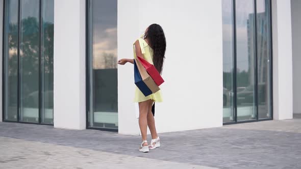 Beautiful Girl Model in a Long Dress After Shopping with Colored Bags in Hands