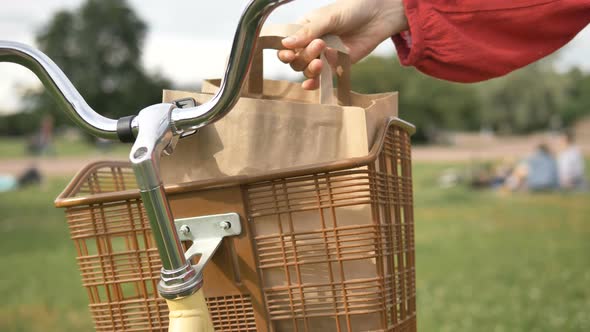 Woman Takes Out a Paper Bag of Food From a Vintage Basket on a Bicycle in a Park, Takeaway Delivery