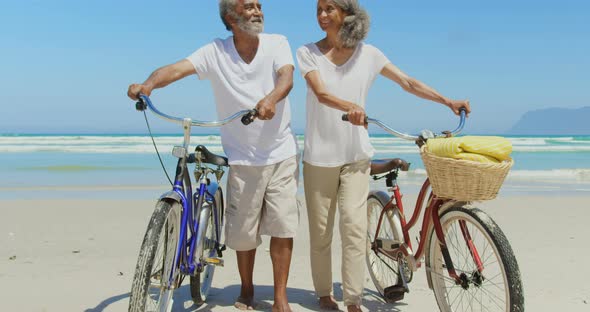 Front view of active senior African American couple with bicycle walking on beach in the sunshine 4k