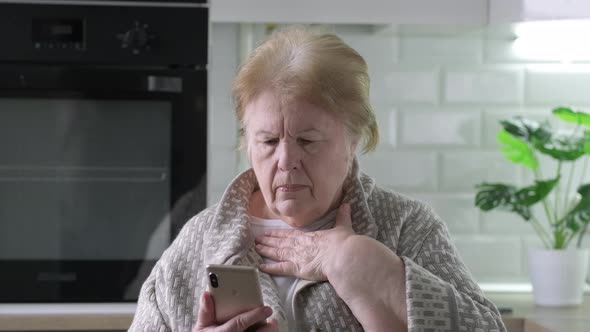 Worried Caucasian Senior Woman at Home Looking at Phone Seeing Bad News or Photos and Shakes Her