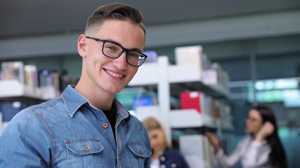 Student At Library Reading Books Near Bookshelves