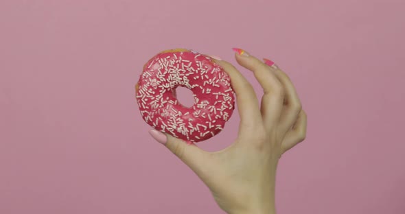 Womens Hand Holding Red, Delicious, Sprinkled Donut on Pink Background.