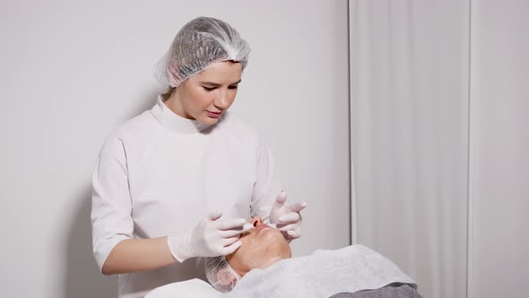 Doctor Beautician Removes Makeup Patient Lying on a Special Table